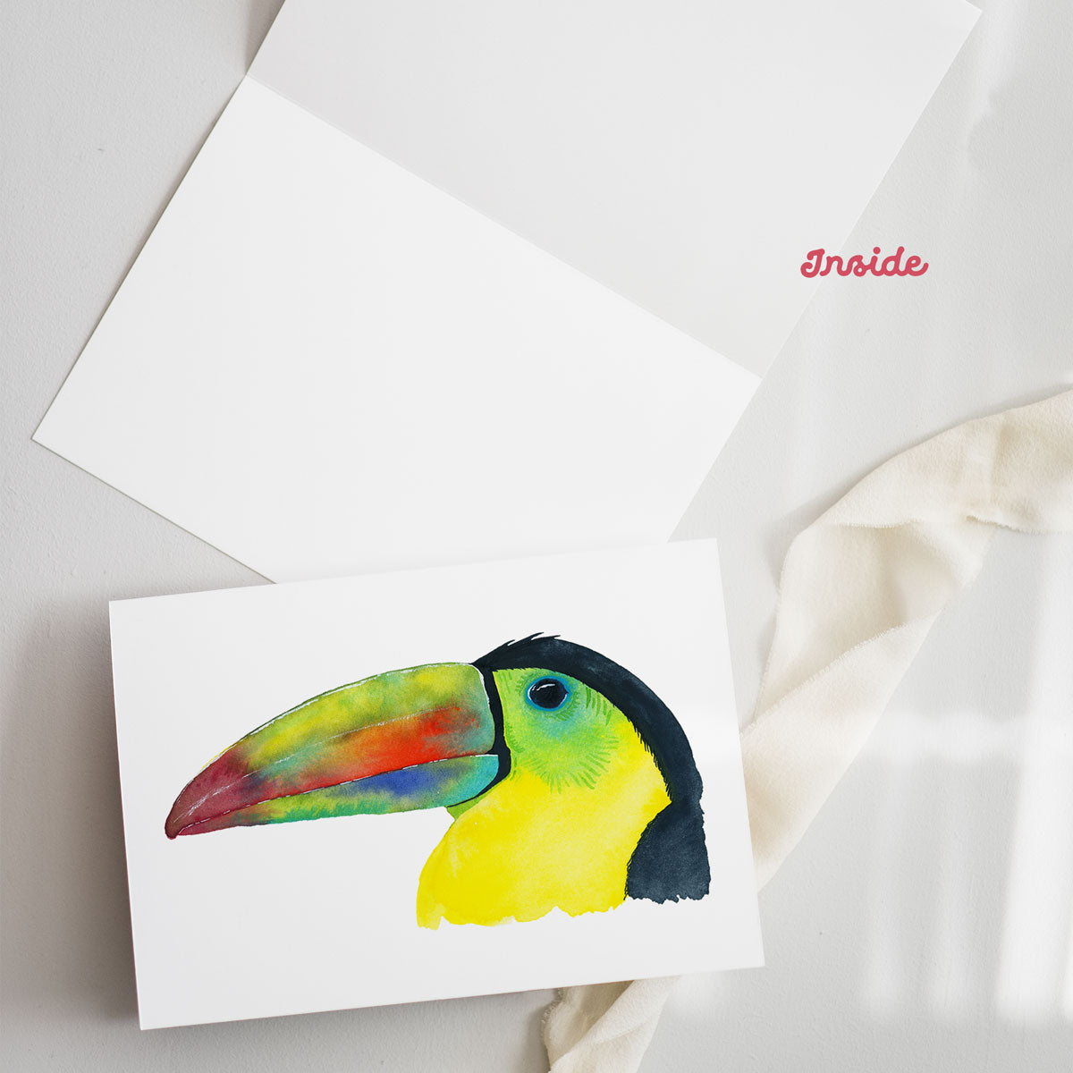 Close-up of a colorful watercolor toucan illustration on a blank greeting card