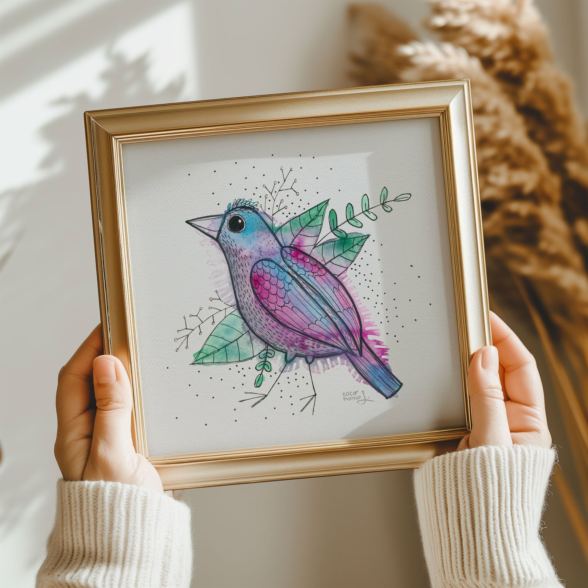 A whimsical and colorful watercolor bird painting in a frame, held by two hands