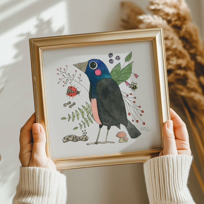 A framed art print featuring a colorful illustration of a common grackle surrounded by nature-inspired details, displayed on a wall.